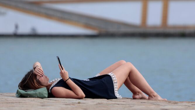 Una mujer descansa e intenta refrescarse junto al Guadalquivir.