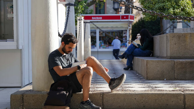 Un joven lee un libro en la Plaza Nueva, enclave principal de la Feria del Libro de Sevilla.