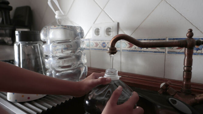 Un cliente de Emasesa llena una garrafa de agua en el grifo de una cocina.