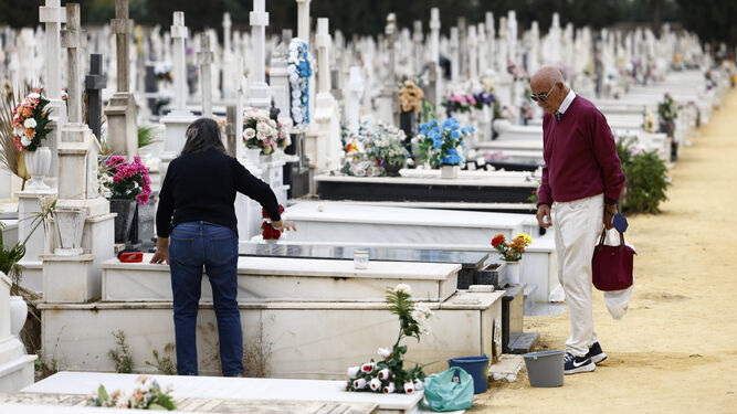Dos personas adecentan una lápida en el cementerio.