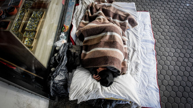 Una persona sin hogar dormita en una calle de la ciudad, arropado por una manta.