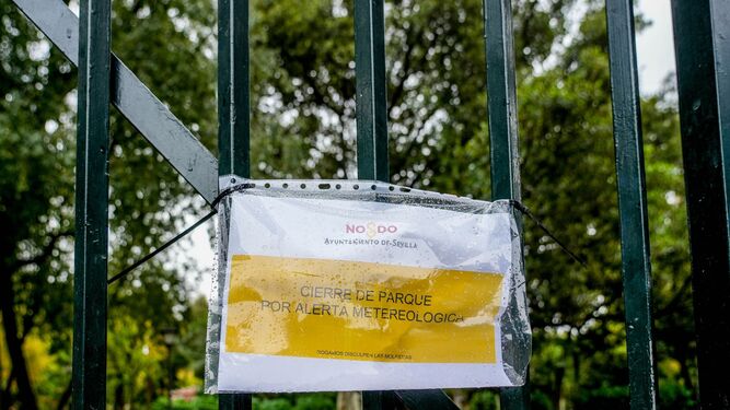 Cartel en una reja de entrada al Parque  de María Luisa que indica el cierre  por alerta meteorológica.