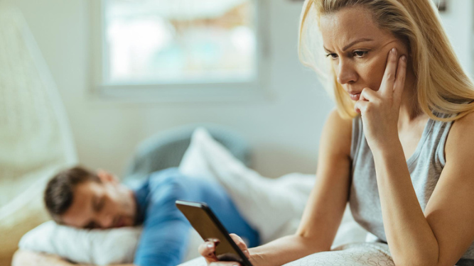 Mujer revisando el móvil de su pareja cuando duerme.