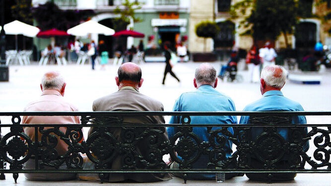 Un grupo de hombres mayores sentados en un banco en una plaza pública.
