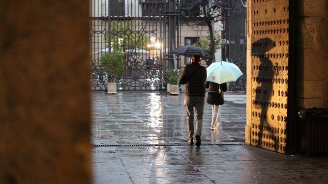 Dos personas con paraguas en el Rectorado de la Universidad de Sevilla.