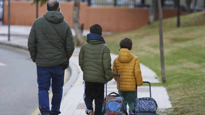 Un padre llevando a sus dos hijos al colegio.
