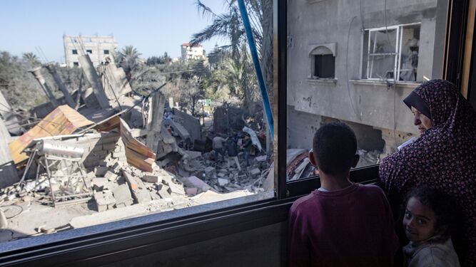 Una familia palestina mira a través de una ventana rota  los restos de un edificio residencial en Jan Yunis.